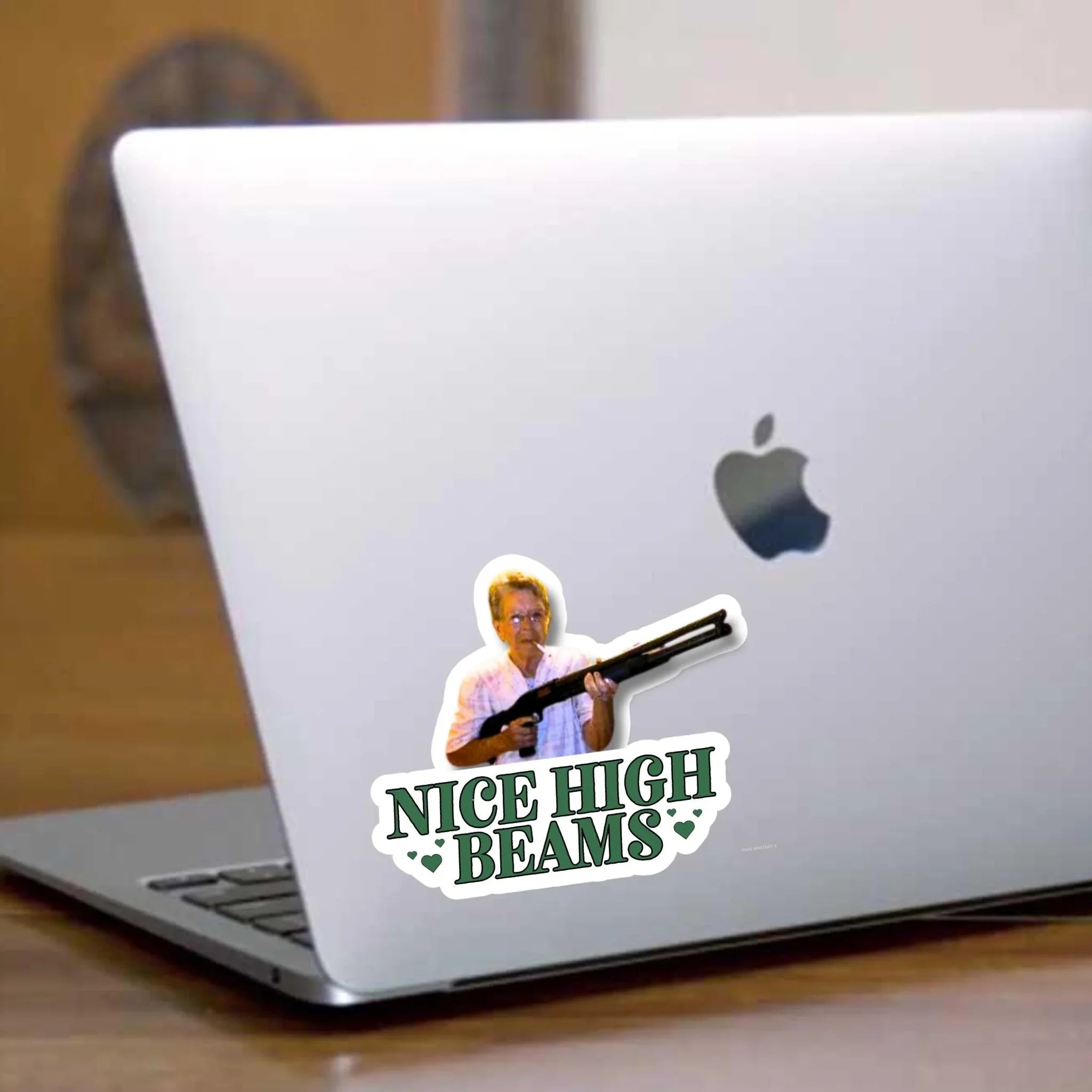 Funny 'Nice High Beams' bumper sticker with man holding shotgun, on silver laptop