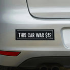 Black and white bumper sticker saying 'THIS CAR WAS $12' on white car trunk
